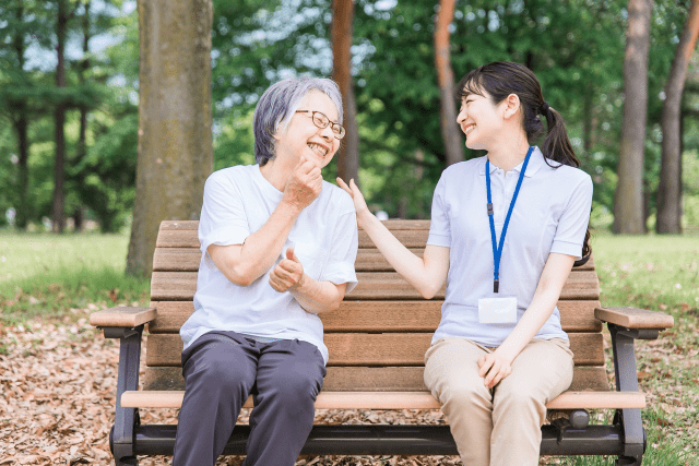公園のベンチで談笑する高齢の利用者と介護スタッフ